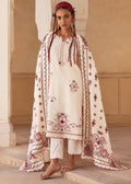 A woman models a traditional South Asian outfit consisting of an off-white embroidered kurta, matching white pants, and a large off-white dupatta with burgundy floral embroidery, set against a warm beige architectural background.