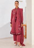 A woman modeling a dusty rose pink ethnic three-piece suit with intricate floral embroidery and border detailing, standing in a bright, modern indoor setting.