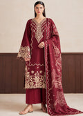 A woman models a traditional Indian salwar kameez suit in deep maroon with intricate beige and gold embroidery. The set includes a long-sleeved tunic with ornate embroidery on the neckline, sleeves, and hem, matching maroon trousers, and a long dupatta featuring floral and bird motifs.