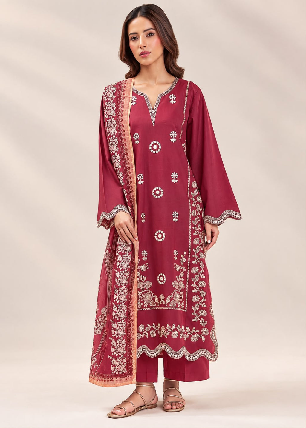 A woman modeling a traditional Indian salwar kameez set in deep maroon, featuring intricate white and gold floral embroidery, a matching dupatta, and matching trousers, set against a neutral beige studio background.