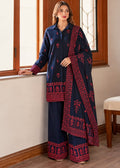 A woman models a navy blue three-piece traditional outfit with deep red and pink floral embroidery, consisting of a long-sleeve kurta, wide-leg trousers, and a matching dupatta, set against an indoor background with wooden window frames.