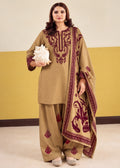 A woman models a traditional three-piece salwar kameez suit in khaki beige with deep maroon embroidery. The set includes a long-sleeve tunic with ornate embroidery on the chest and sleeves, matching wide-leg trousers with small embroidered motifs near the hems, and a coordinating dupatta featuring a large floral print and border design.