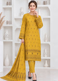A woman models a three-piece mustard yellow ethnic salwar kameez suit with matching dupatta. The kurta and trousers feature delicate black geometric embroidery, and the dupatta has a matching border print.