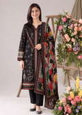 A woman modeling a black three-piece ethnic suit with intricate multicolor paisley and floral patterns, featuring a matching dupatta, black pants, and black shoes, set against a studio backdrop with floral arrangements.