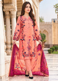 A woman models a peach-colored three-piece salwar kameez suit with floral embroidery and a matching magenta dupatta, set against a classical stone archway background.