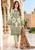 A woman models a traditional three-piece salwar kameez suit in sage green, featuring intricate floral embroidery, paired with matching trousers and a brown patterned dupatta, set against a historic stone archway background.