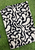 A folded garment or fabric piece with an abstract black and off-white organic pattern, laid flat on green grass.