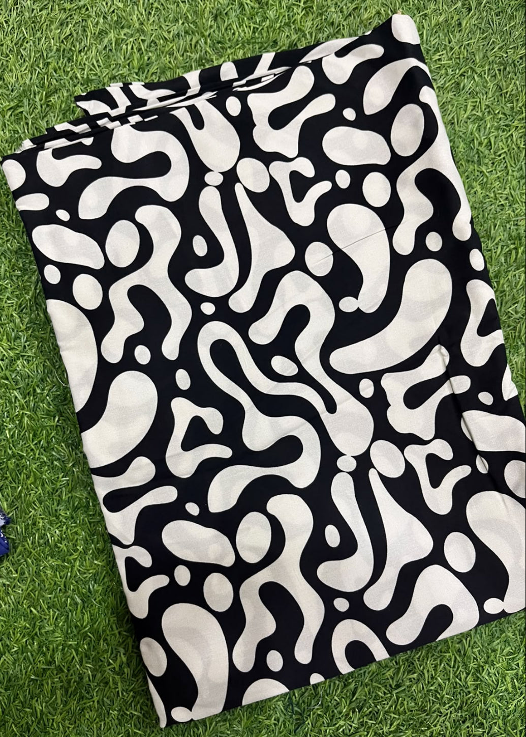 A folded garment or fabric piece with an abstract black and off-white organic pattern, laid flat on green grass.