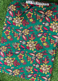 A folded piece of green fabric with a colorful floral block print pattern, laid flat on a green grass background. The print features yellow, pink, and red flowers with blue and brown details.