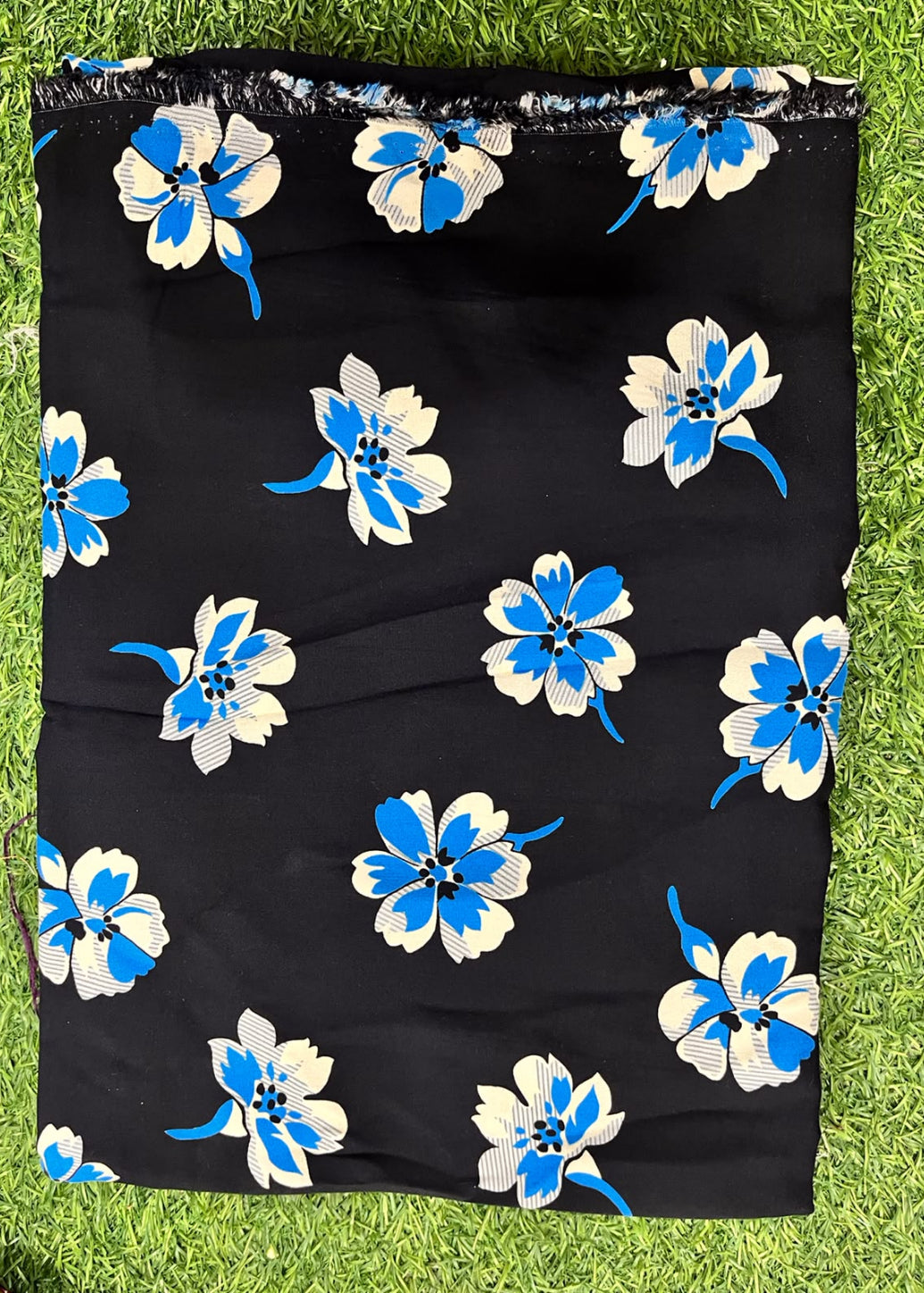 Black fabric with a blue and white floral print, laid flat on green grass.