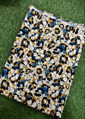 A folded fabric yardage with a bold floral pattern in mustard yellow, white, black, and blue, laid flat on green grass.