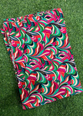A folded piece of fabric with a vibrant, multicolored abstract swirl pattern, laid flat on green grass.