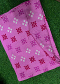 A pink fabric item, likely a scarf or sari, featuring a repeating pattern of magenta and white floral snowflake motifs, laid flat on a green artificial grass background.