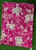 A folded magenta pink fabric with a cream floral and vine pattern, laid flat on green grass.