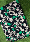 A folded piece of fabric with a bold geometric floral print in black, white, and green, laid flat on a green grass-like surface.