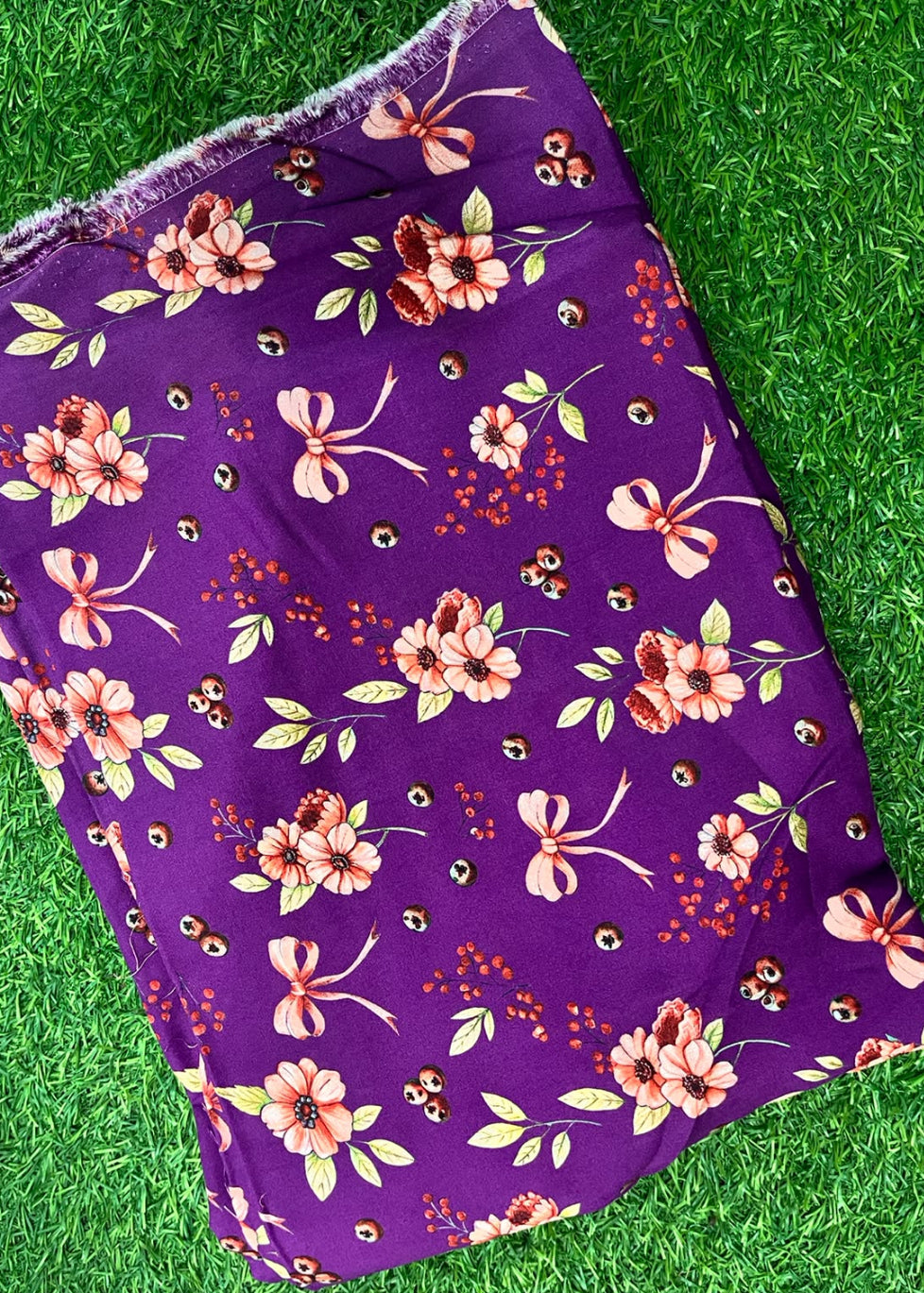 Purple floral fabric with pink hibiscus flowers, green leaves, and small orange-red berry clusters, laid flat on green grass.