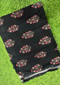 Black fabric with pink and red floral block prints, laid flat on a green grass background.