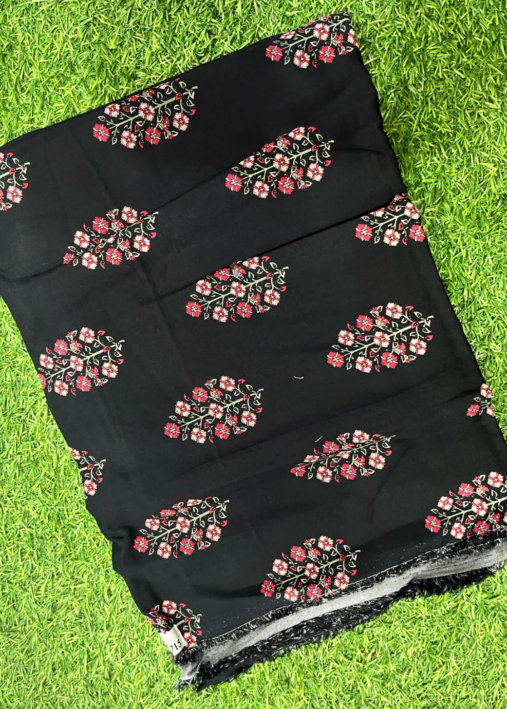 Black fabric with pink and red floral block prints, laid flat on a green grass background.