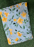 A folded piece of light blue fabric with a yellow and green floral print, laid flat on a green grass background.