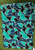 A folded piece of fabric with a bold abstract floral pattern in teal, navy, black, and white, laid flat on green grass.