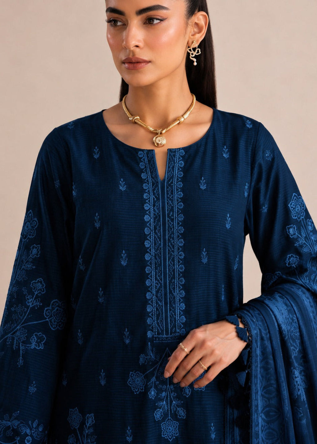 A woman modeling a dark navy blue embroidered kurta with matching dupatta, featuring intricate floral and geometric patterns, set against a solid beige background.
