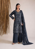 A woman models a dark navy blue ethnic salwar kameez suit with intricate white embroidery, matching wide-leg trousers, and a sheer embroidered dupatta, standing against a neutral beige background with a decorative hanging reed arrangement.