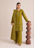 A woman models a three-piece olive green ethnic suit with matching dupatta, featuring gold embroidery on the kurta and trousers, standing next to a stack of terracotta pots against a beige studio background.