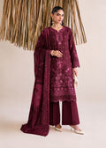 A woman models a three-piece traditional outfit in deep maroon with floral embroidery, featuring a long kurta, wide-leg pants, and a matching dupatta, set against a neutral studio backdrop with a decorative gold hanging.