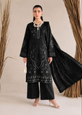 A woman models a black traditional South Asian outfit with intricate silver embroidery, wide-leg pants, a matching black dupatta, and a statement necklace, set against a neutral beige background with dried palm branches.