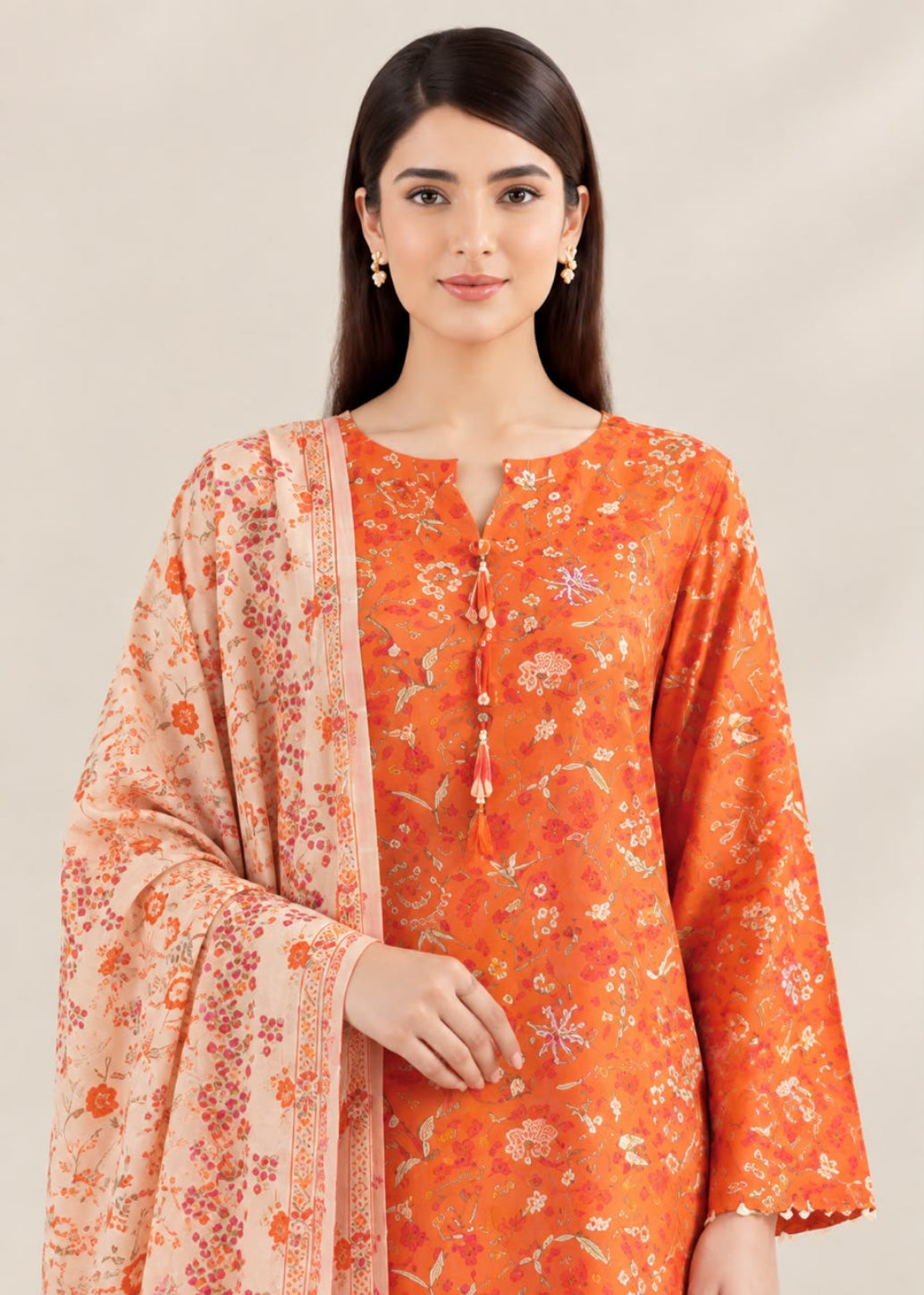 A woman modeling a traditional Indian outfit featuring a bright orange kurta with delicate floral prints and a peach-colored dupatta with a matching floral pattern, set against a plain beige background.
