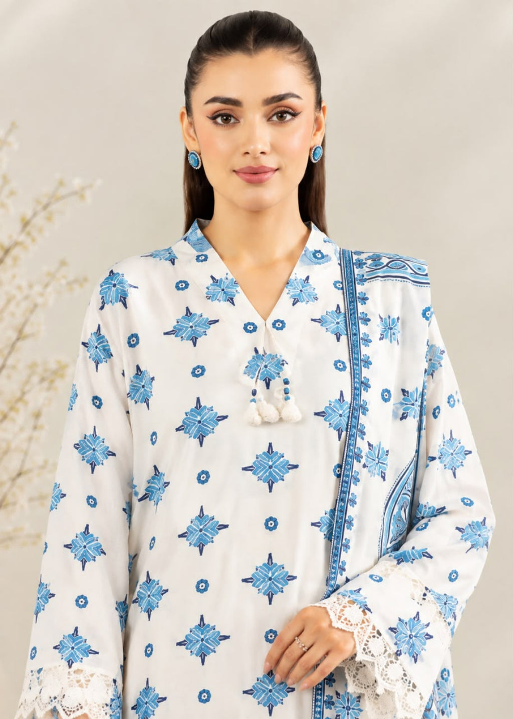 A woman modeling a white kurta with blue starburst and floral block prints, featuring a V-neckline with tassel ties and a matching blue patterned dupatta.