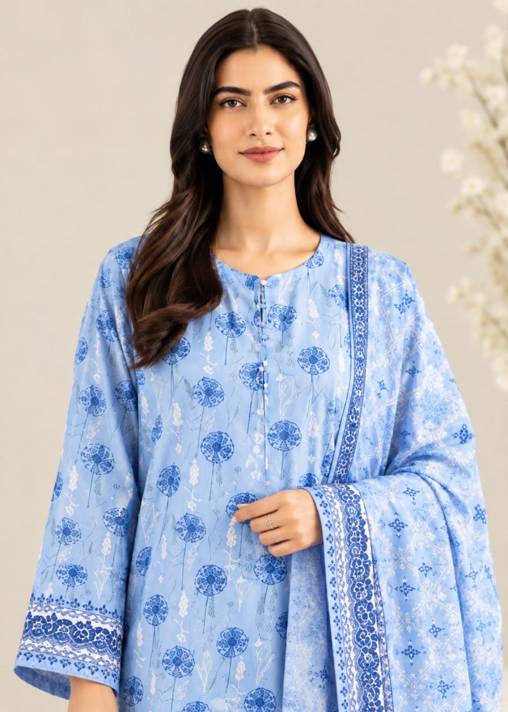 A woman modeling a light blue kurta with blue floral block prints and a matching dupatta, set against a soft beige background with subtle white floral details.