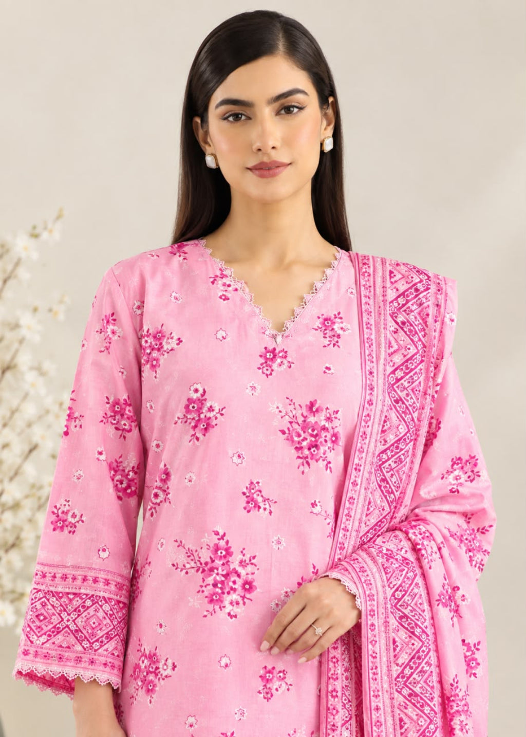 A woman modeling a pink traditional outfit with floral embroidery and a matching embroidered dupatta, set against a soft beige background.