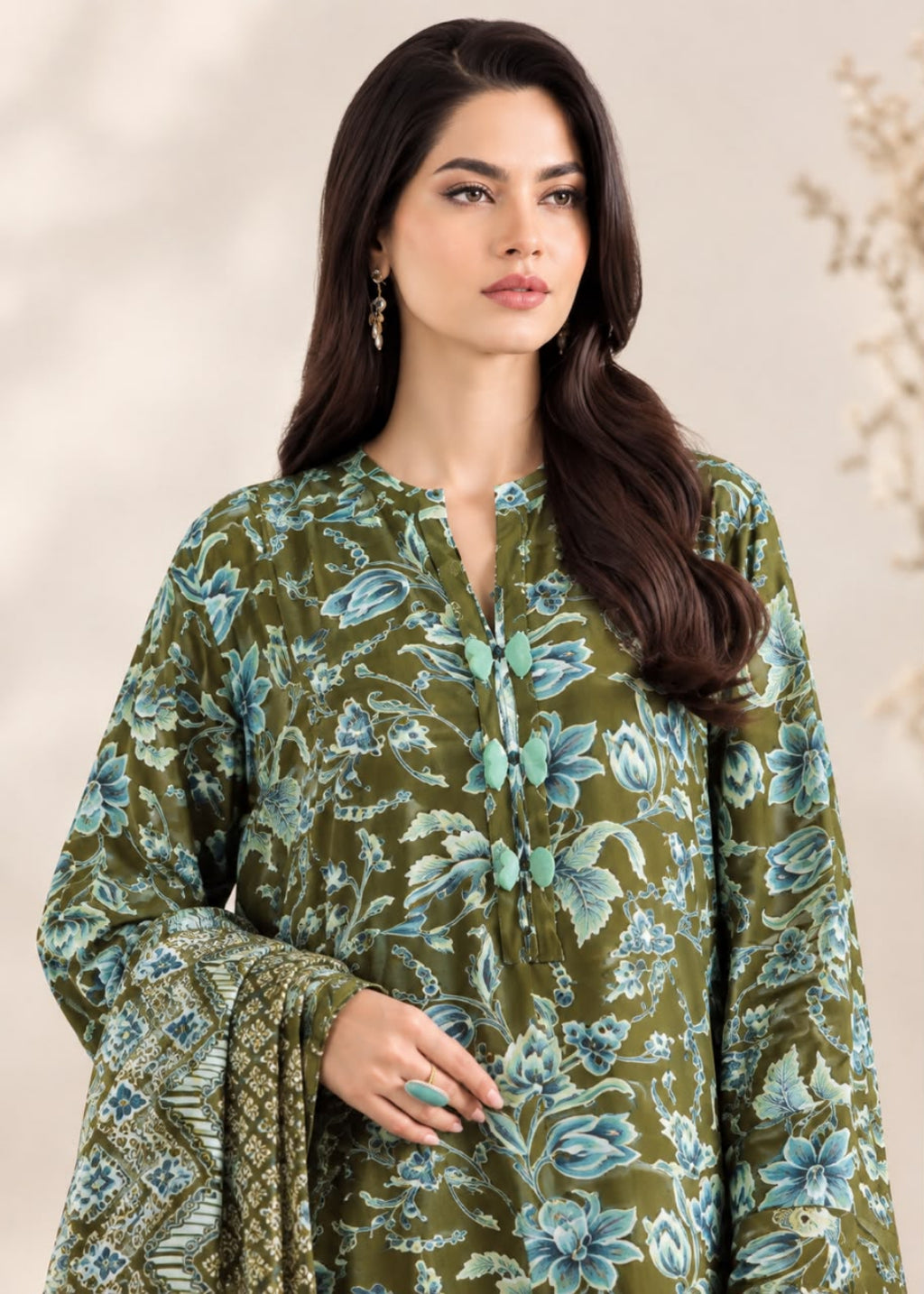 A woman modeling a green printed kurta with blue and teal floral motifs, paired with a matching patterned dupatta, set against a soft beige background.