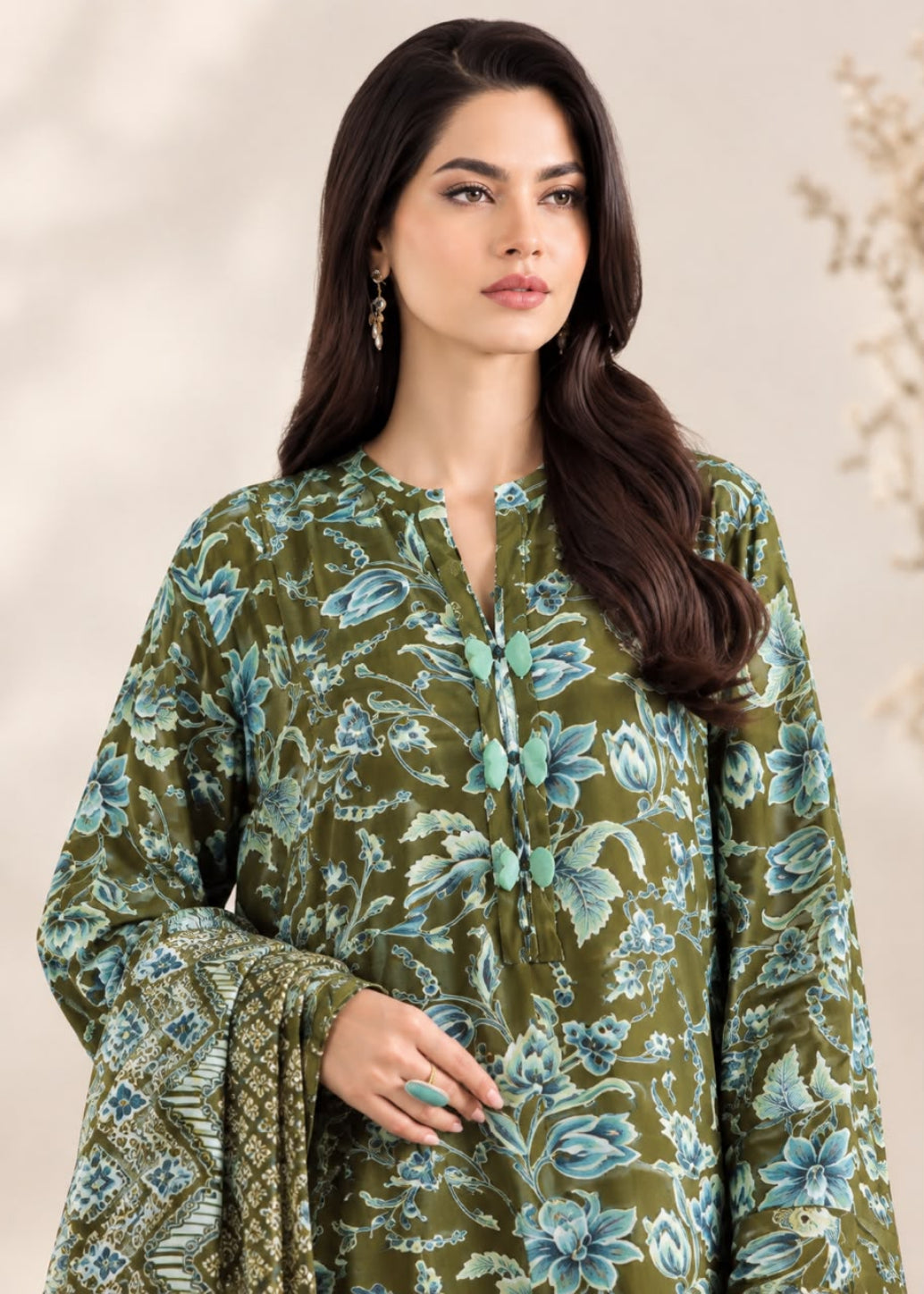 A woman modeling a green printed kurta with blue and teal floral motifs, paired with a matching patterned dupatta, set against a soft beige background.