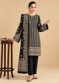 A woman models a black long kurta with intricate beige and gold embroidery, paired with black trousers, standing next to a wooden stool against a beige background.