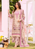 A woman models a traditional three-piece salwar kameez suit in a light beige/cream color with pink and purple floral embroidery and prints, set against a soft pink garden backdrop.