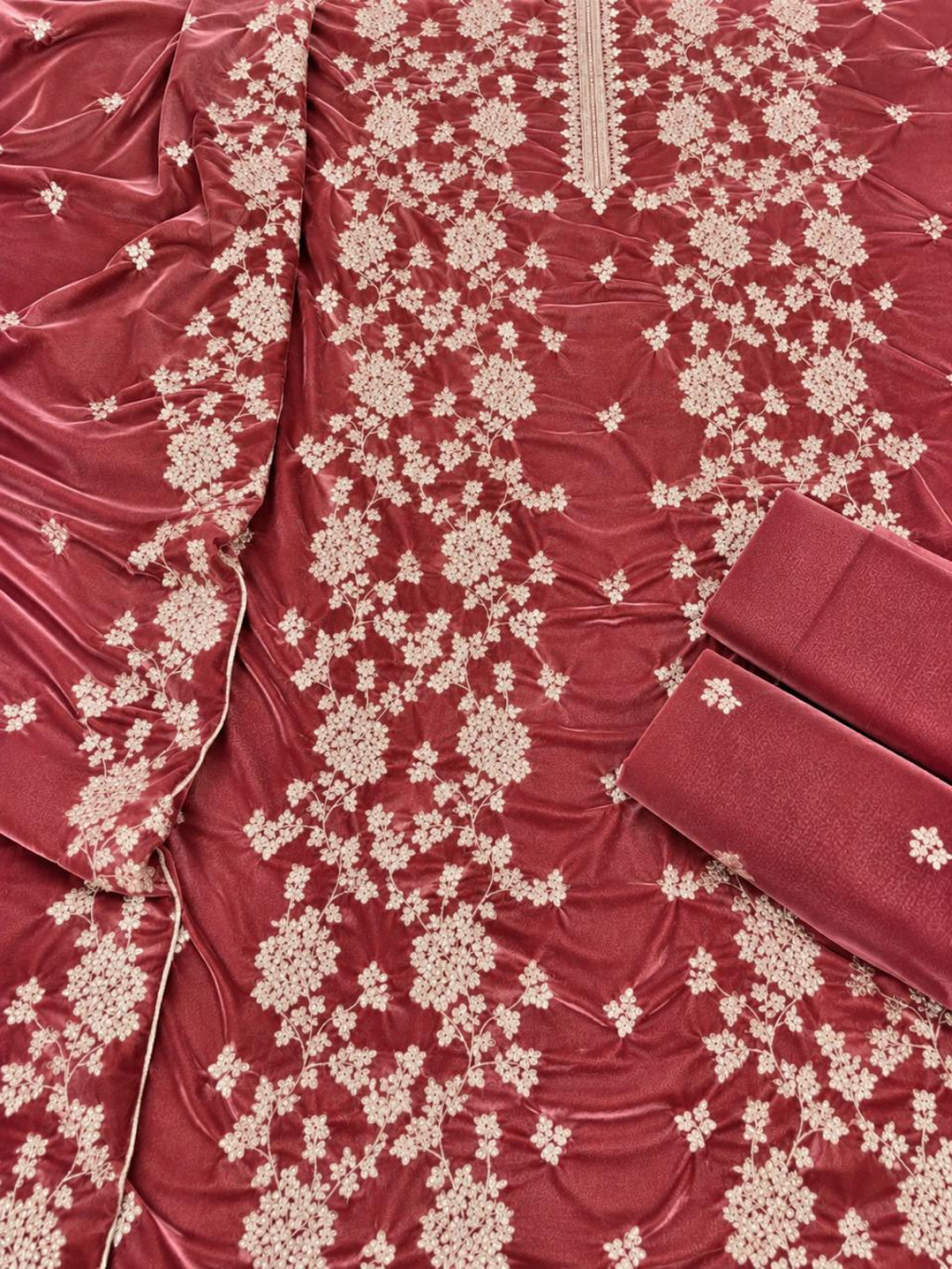 A close-up of a maroon velvet fabric garment or textile with dense cream floral embroidery and a matching folded fabric piece on a plain background.