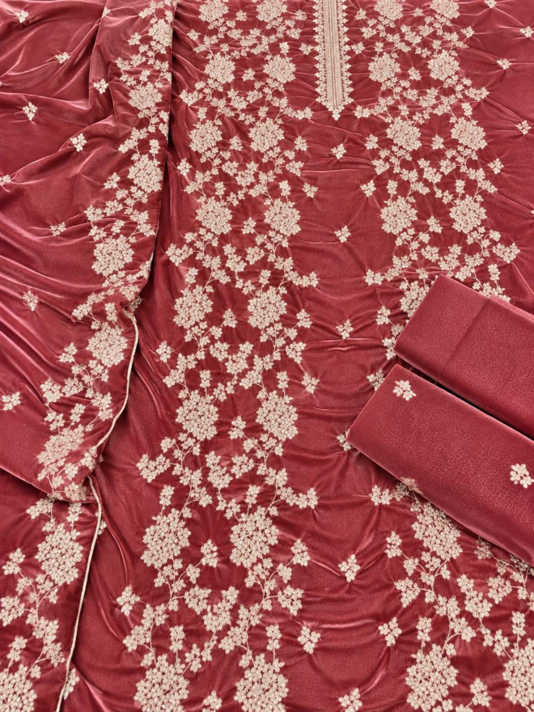 A close-up of a maroon velvet fabric garment or textile with dense cream floral embroidery and a matching folded fabric piece on a plain background.