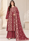 A woman models a traditional Indian salwar kameez suit in maroon velvet with beige floral embroidery, featuring a long kurta, matching wide-leg pants, and a draped dupatta.