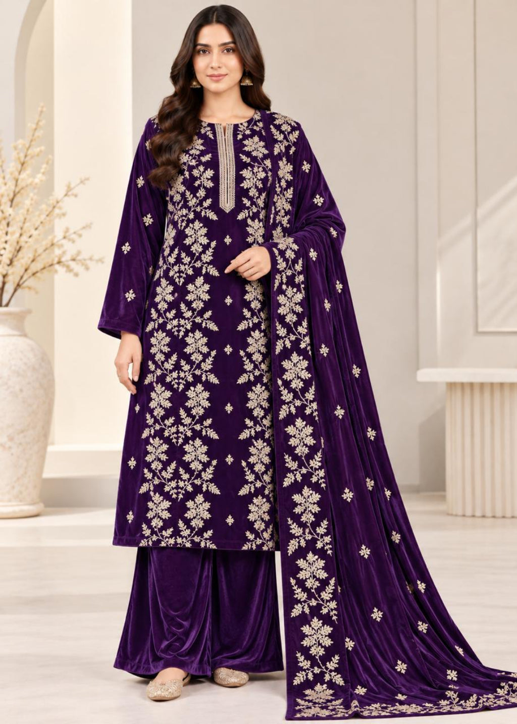 A woman models a deep purple velvet three-piece traditional outfit with intricate silver floral embroidery, consisting of a long kurta, matching pants, and a draped dupatta, set against a neutral indoor background.