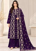 A woman models a deep purple velvet three-piece traditional outfit with intricate silver floral embroidery, consisting of a long kurta, matching pants, and a draped dupatta, set against a neutral indoor background.