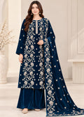 A woman models a navy blue velvet salwar kameez suit with intricate silver floral embroidery, matching wide-leg trousers, and a long draped dupatta, set against a neutral indoor background.