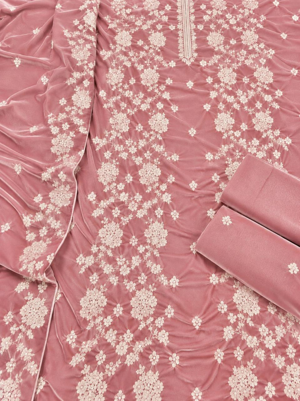 A close-up of a dusty rose pink fabric garment or textile with an allover cream floral embroidery pattern, featuring a folded matching fabric piece on the right side.