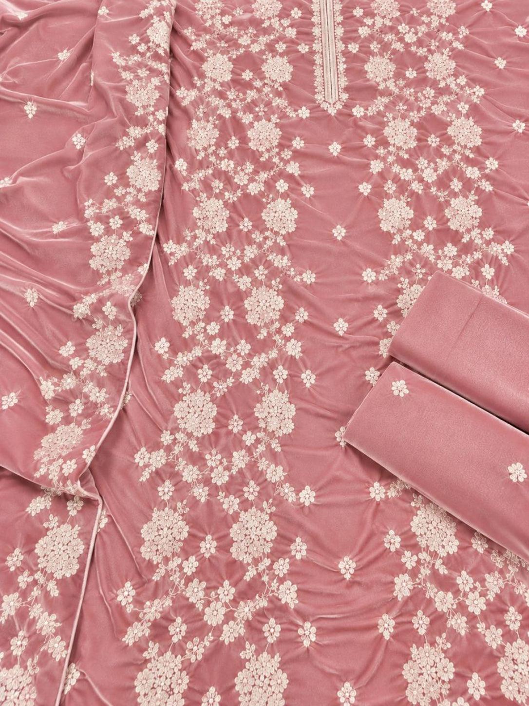 A close-up of a dusty rose pink fabric garment or textile with an allover cream floral embroidery pattern, featuring a folded matching fabric piece on the right side.