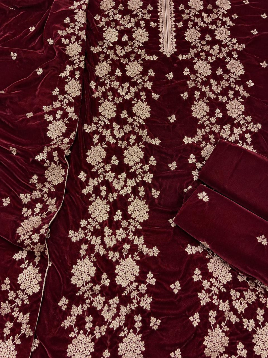 A close-up of a deep maroon velvet fabric with intricate beige floral embroidery and a matching embroidered inner lining.