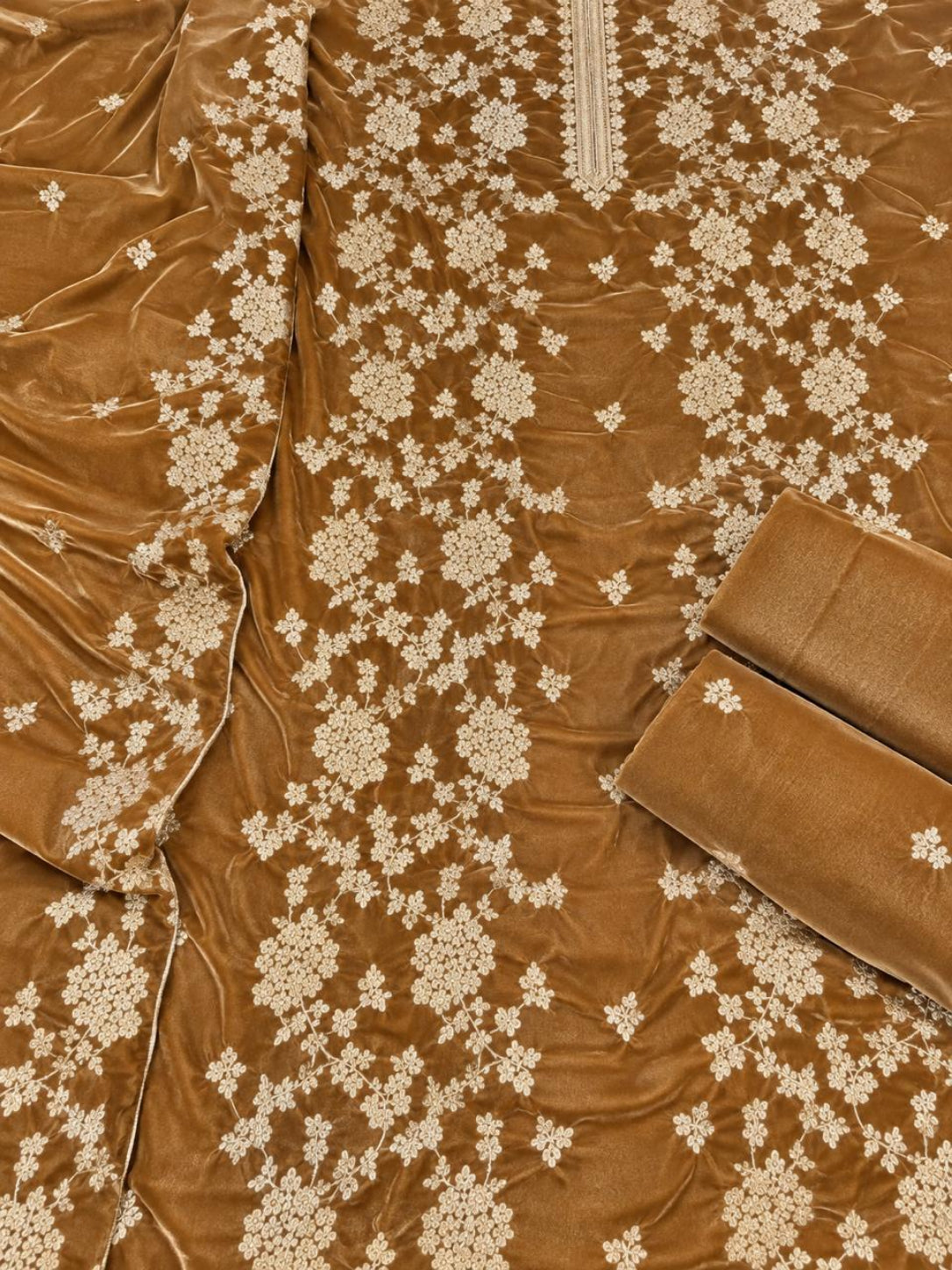A close-up of a brown velvet fabric garment or textile with cream floral embroidery and matching rolled fabric pieces.