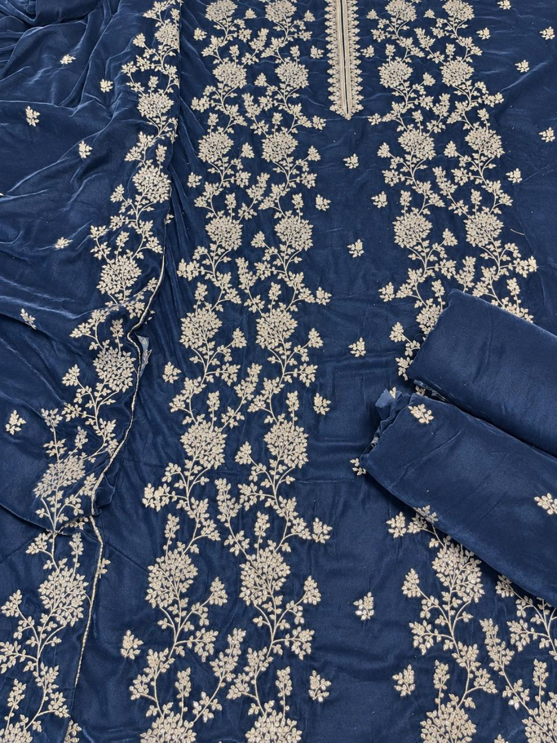A close-up of a navy blue fabric garment or textile with extensive cream floral embroidery and a matching rolled fabric piece on the right side.