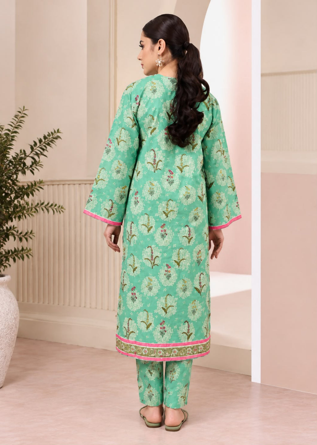 A woman shown from the back wearing a mint green printed kurta and matching pants with pink and gold border details, standing in a softly lit indoor setting.