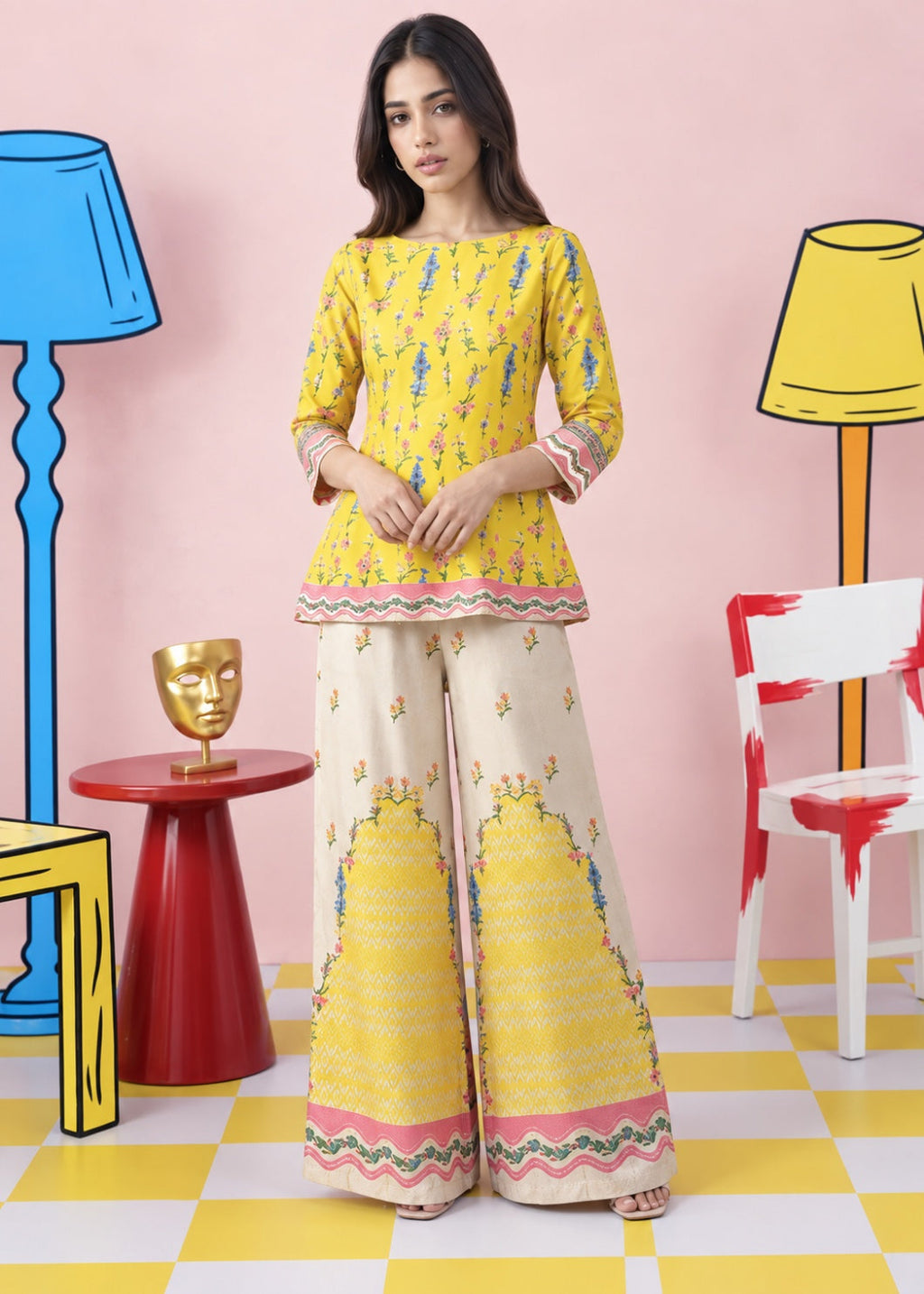 A woman models a traditional three-piece salwar kameez set featuring a yellow printed kurta, a cream-colored printed kameez, and matching wide-leg trousers, set against a whimsical pink background with cartoon-style props.